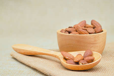 Almond in wooden spoon on sackcloth background, selective focus.