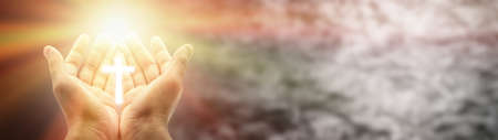 Hands holding a Christian cross on a blurred background with copy space