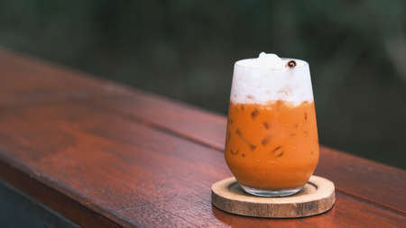 Thai Milk Tea, Milk ice tea, Cheddar is a traditional Thai drink that has long been popular, fresh and sweet dessert on a wooden saucer, vintage wooden table in cafe.の写真素材