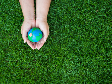 earth in hands and green grass field background. environment save earth concept.の写真素材