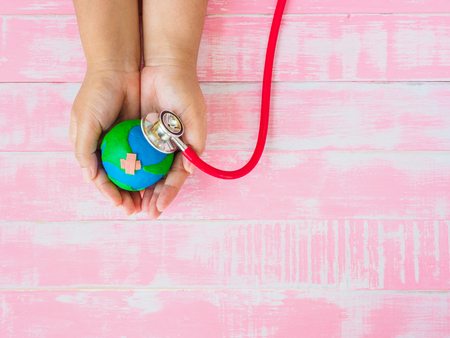 World Earth Day April 22 and World health day, April 7 concept. Woman hand holding handmade earth with Stethoscope on pink wooden table background texture.の写真素材