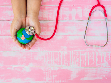 World Earth Day April 22 and World health day, April 7 concept. Woman hand holding handmade earth with Stethoscope on pink wooden table background texture.の写真素材