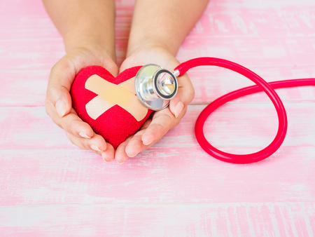 Health and medical, love and valentine concept. Red heart on a woman hand with red stethoscope on the pink wood backgroundの写真素材