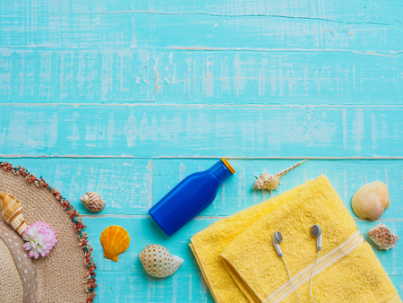 Beach accessories including sunscreen, hat beach, shell, yellow towel and earphones on bright blue pastel wooden background for summer holiday and vacation concept.の写真素材