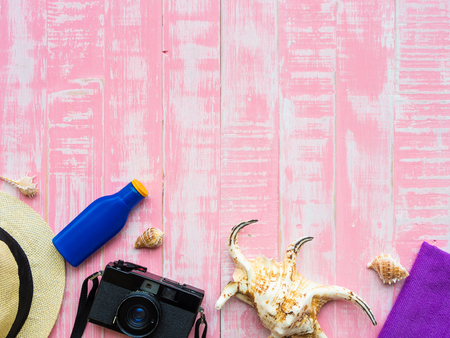 Beach accessories including sunscreen, hat beach, shell and retro camera on bright pink pastel wooden background for summer holiday and vacation concept.の写真素材