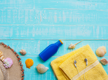 Beach accessories including sunscreen, hat beach, shell, yellow towel and earphones on bright blue pastel wooden background for summer holiday and vacation concept.の写真素材