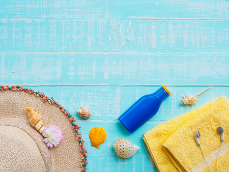 Beach accessories including sunscreen, hat beach, shell, yellow towel and earphones on bright blue pastel wooden background for summer holiday and vacation concept.の写真素材