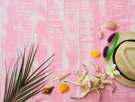 Beach accessories including sunscreen, hat beach, shell and coconut leaves on bright pink pastel wooden background for summer holiday and vacation concept.の写真素材