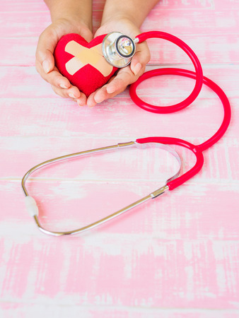 Health and medical, love and valentine concept. Red heart on a woman hand with red stethoscope on the pink wood backgroundの写真素材