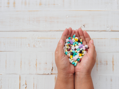 Woman hands holding colorful pills on white wooden background. Healthcare and medical concept.の写真素材