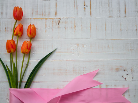 mother's day concept. tulips flower and pink ribbon on white wooden background.の写真素材