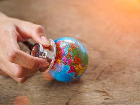 woman hand holding stethoscope with globe on wooden texture background. save earth, save environment concept.の写真素材