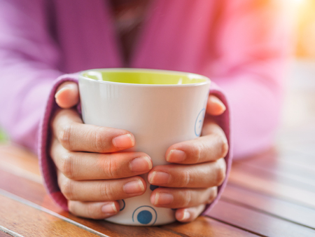 Female hand holding a cup on wooden table.の写真素材