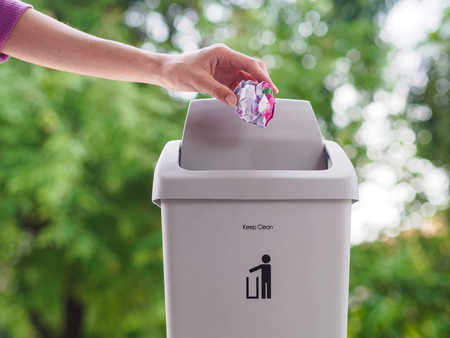 female hand trowing a paper into a garbage bin on bokeh background. cleaning concept.の写真素材