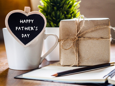 Happy fathers day concept. coffee cup with gift box, heart tag with HAPPY FATHER'S DAY text, notebook and glasses on wooden table background.の写真素材