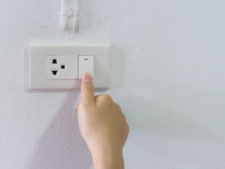 Close up female hand turning on or off on grey light switch with texture background. Turning light concept.の写真素材