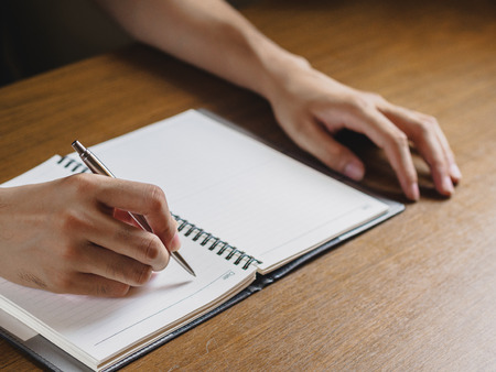 Close up of man's hands writing in notebook placed on wooden desktop. business, Education concept.