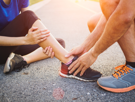 Ankle sprained. Young woman suffering from an ankle injury while exercising and running and she getting help from man touching her ankle. Healthcare and sport concept.の写真素材