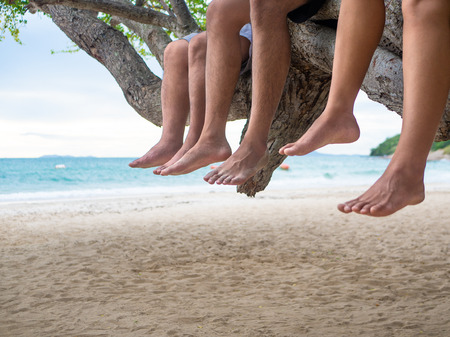 Legs hanging on the tree branch beside the sea beach background. Vacation, Holiday, Summer, Friendship Concept.の写真素材