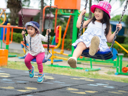 Two Happy little girls playing swing at the playground. Happy, Family, Sister Concept.の写真素材