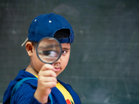 The boy holding the magnifying glass in front of blackboard. Back to School, Education Concept.の写真素材