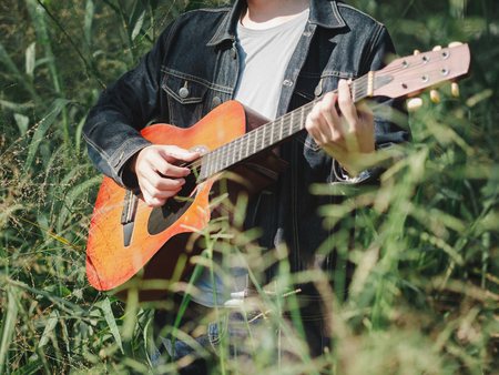 handsome musician playing acoustic guitar at the grass field blur background. World music day. music and instrument concept.の写真素材