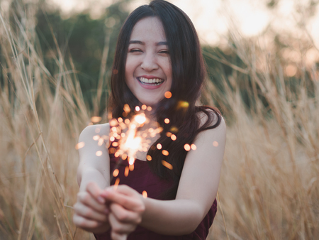 Happy cute girl holding a sparkler in the dry grass field for celebrate.