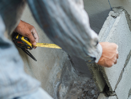 professional construction worker uses measuring Tape for measure and laying bricks with cement.の写真素材