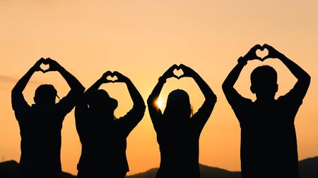 A group of people with raised arms and make hand to the heart shape looking at sunrise on the mountainの写真素材
