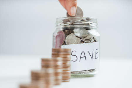women hand putting money coin into glass jar for saving money. saving money and financial conceptの写真素材