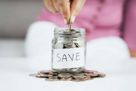 women hand putting money coin into glass jar for saving money. saving money and financial conceptの写真素材