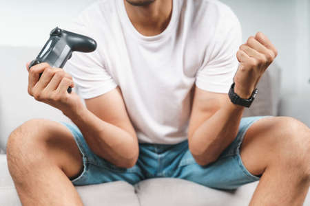 Excited young handsome man playing video game and raising fists sitting on the couch at home.
