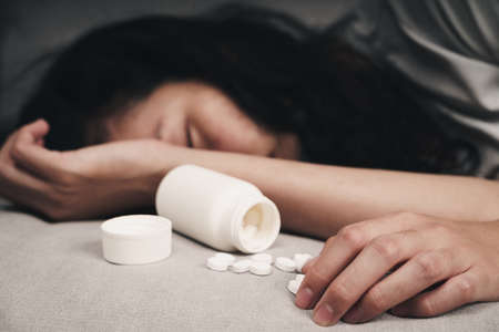 Woman taking medicine overdose and lying on the couch with open pills bottle. overdose and suicide Concept.の写真素材
