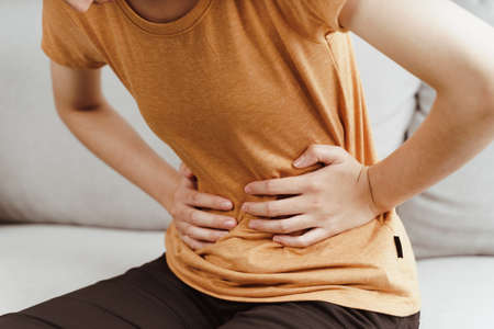 Young woman suffering from strong abdominal pain sitting on the couch at home. Gastritis, Period, menstruation.の写真素材