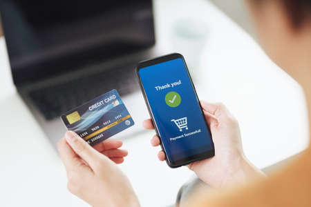 Young woman holding credit card and using smart phone for online shopping, internet banking, e-commerce, spending money, working from home conceptの写真素材