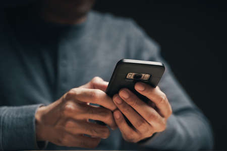 Closeup of a man using a smartphone on the wooden table, searching, browsing, social media, message, email, internet digital marketing, online shopping.の写真素材