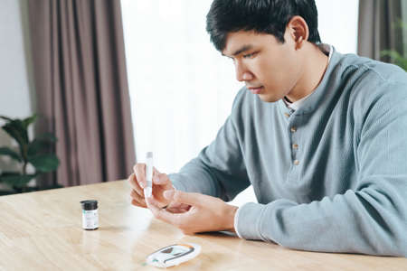 Asian man using lancet on finger for checking blood sugar level by Glucose meter, Healthcare and Medical, diabetes, glycemia conceptの写真素材