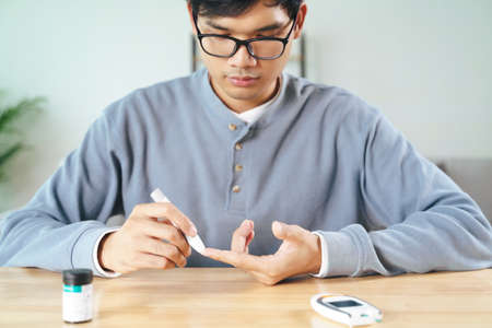Asian man using lancet on finger for checking blood sugar level by Glucose meter, Healthcare and Medical, diabetes, glycemia conceptの写真素材