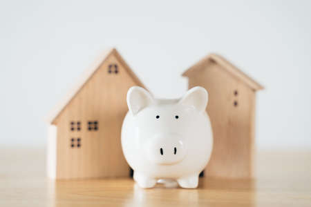 Wooden house with white piggy bank on wooden table. saving money for buying house, financial plan home loan concept.の写真素材