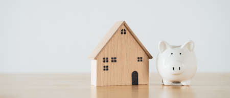 Wooden house with white piggy bank on wooden table. saving money for buying house, financial plan home loan concept.の写真素材