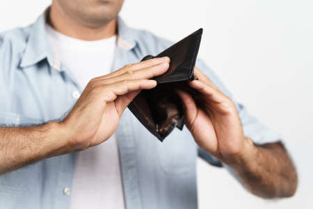 Upset man holding upside down and looking inside his empty wallet on white background. financial crisis, bankruptcy, no money, bad economy Concept.の写真素材