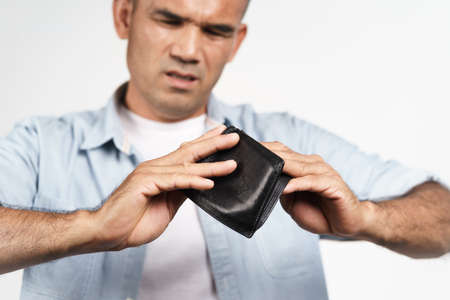 Upset man holding upside down and looking inside his empty wallet on white background. financial crisis, bankruptcy, no money, bad economy Concept.の写真素材