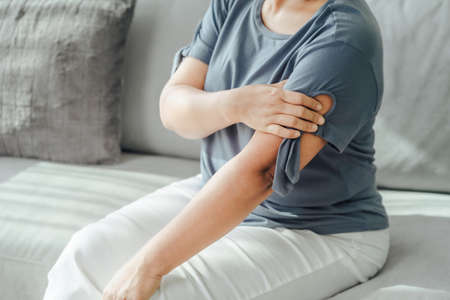 Arms Pain. Woman Suffering From Painful Feeling In Arm Muscles sitting on the sofa. Healthcare and...