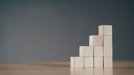 Pile of wooden cube block stack as stair step on wood table. Success, climbing to the top,...