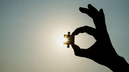 Silhouette closeup of hand holding a piece of jigsaw puzzle over sunlight effect. symbol of association and connection concept. business strategy.の写真素材