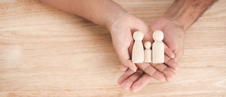 Man husband and Woman wife hands holding wooden peg dolls on the wood table background. family home, foster care, homeless charity support concept, family mental health.の写真素材