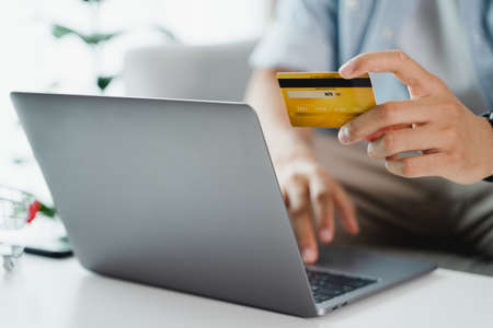 Hand holding credit card and using laptop. Businessman or entrepreneur working from home. Online...