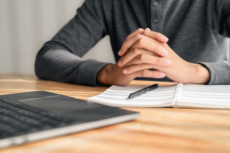 Close up of man clasped hands clenched together on table, businessman preparing for job interview, concentrating before important negotiations, thinking or making decision, business conceptの写真素材