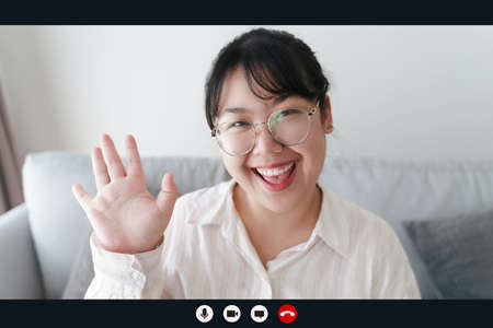 Portrait happy woman working at home by video conference meeting waving hand, talking and looking at...