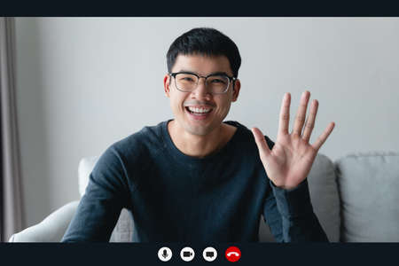Portrait happy man working at home by video conference meeting waving hand, talking and looking at...
